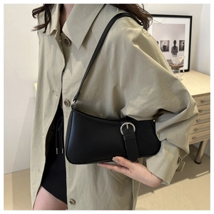 Detail of minimalist black baguette bag with silver buckle worn on the shoulder