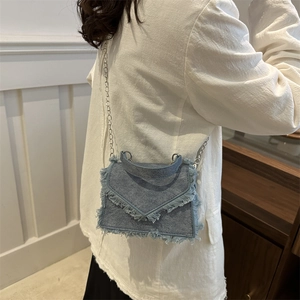 Blue denim mini crossbody bag with fringe edges and silver chain strap on model