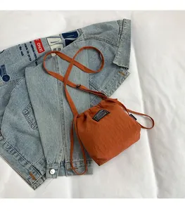 Detail of orange drawstring crossbody bucket bag with black FASHION label on denim