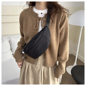 Minimalist black crossbody sling bag with adjustable strap worn by model in a soft home setting
