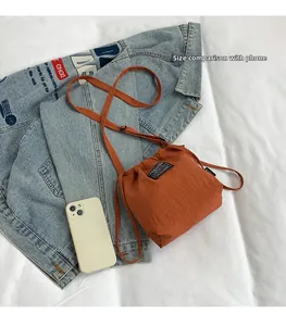Detailed size comparison of orange drawstring mini bag next to a smartphone and denim jacket