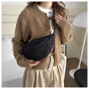 Detail of a black nylon crossbody bag worn with an oversized brown cardigan sweater