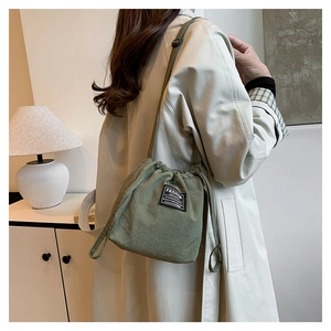 Detail view of a green drawstring bucket bag with a fashion label and thin crossbody strap