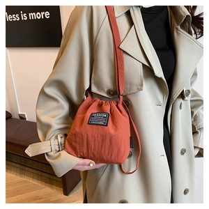 Detail of orange nylon bucket bag with drawstring and Fashion Instinct label on a model