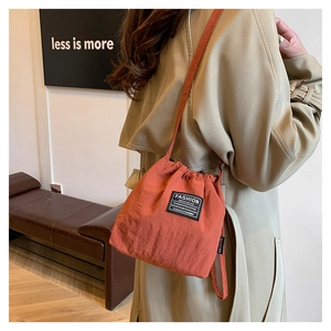Detail view of brick orange drawstring bucket bag with fashion label and thin strap