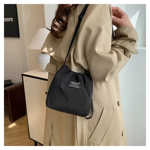 Detail of black drawstring bucket bag with fashion label on modern beige trench coat
