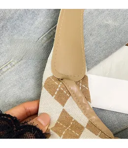 Detailed view of checkered canvas handbag featuring reinforced stitching and brown leather strap