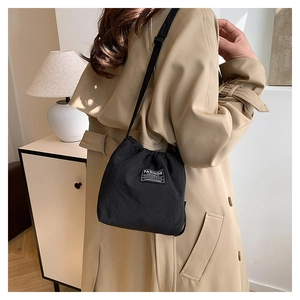 Detail of a black drawstring bucket bag worn over a beige coat for daily commute