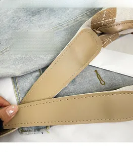 Detail of precise white stitching on light blue denim and brown plaid tote bag strap