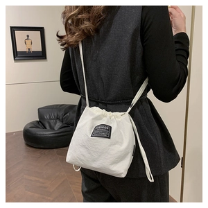 Detail of white drawstring bucket bag showing fashion patch and nylon texture on model