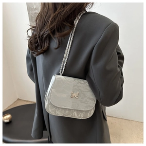 Detail of silver textured leather shoulder bag with a metallic butterfly clasp on strap