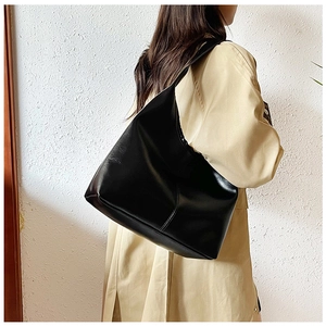Side view of a sleek black PU leather tote bag worn by a model in a beige trench coat