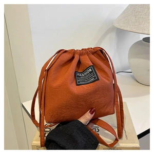 Detail of burnt orange drawstring bucket bag featuring a woven label on a nylon surface