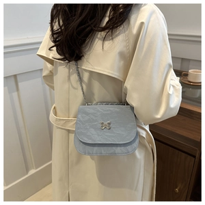 Light blue crossbody flap bag with pleated texture and silver butterfly on a model