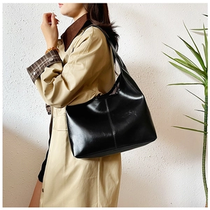 Detail showing high-capacity black shoulder bag with glossy leather and vertical stitching