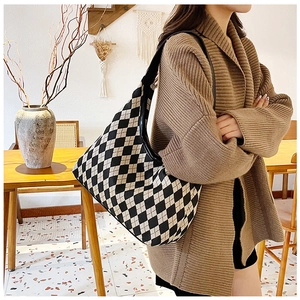 Detailed close-up of a knitted checkerboard tote bag with black leather shoulder strap