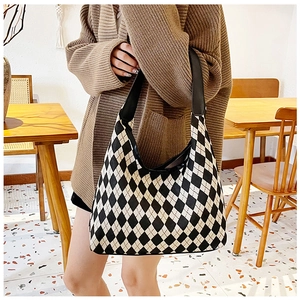 Detail of a large knitted checkered tote bag shown in a cozy coffee shop setting