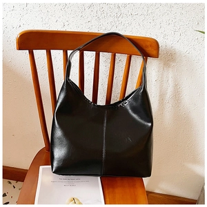 Detail of a black oily faux leather hobo bag with vertical stitching on a wooden chair