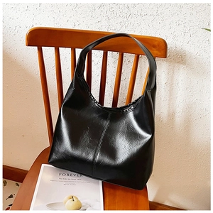 Detail of glossy black leather tote bag featuring sleek vertical seam and hobo design