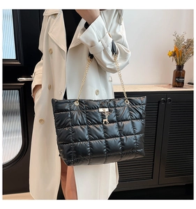 Detail of black quilted tote bag with gold chain strap and deer charm on white coat
