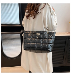 Detail of black quilted tote bag with golden chain strap and deer charm on beige coat
