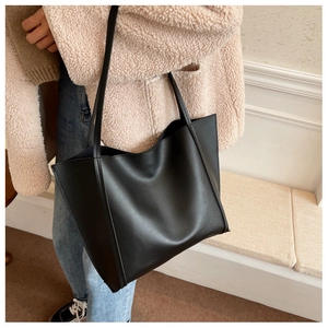 Detailed side view of a large black matte leather tote bag worn over a pink fleece jacket