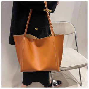 Brown faux leather tote bag with vertical stitching and slim straps worn by a model