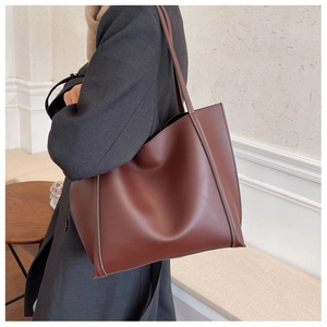Detail view of a large brown faux leather tote bag worn with a wool winter coat
