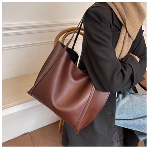 Detail of dark brown leather tote bag with slender straps worn over a black winter coat