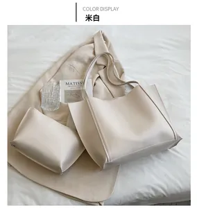 Detailed view of cream leather tote bag and matching pouch on a white fabric background