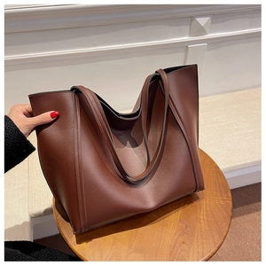 Detail of large dark brown tote bag in matte synthetic leather on a wooden stool
