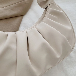 Detail of creamy pleated crescent bag showing fine PU leather texture and knot design
