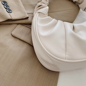 Detailed view of beige ruched pleated shoulder bag on a khaki blazer background