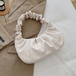 Detail of cream white pleated crescent bag with cloud-style ruched handle on textured fabric