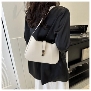 Close-up of beige leather underarm bag with metal buckle shown on model in office setting