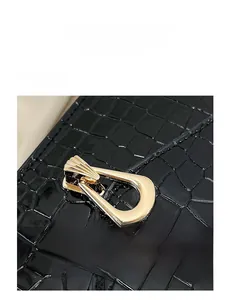 Detail of glossy black crocodile texture leather bag with a gold fan-shaped metal lock