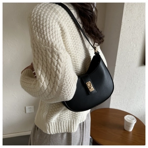 Détail d'un sac hobo en cuir mat noir avec boucle dorée porté à l'épaule pour femme