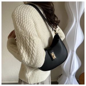 Détail du sac baguette demi-lune en cuir noir avec boucle dorée sur l'épaule du mannequin