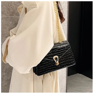 Detail of black crocodile texture bag with gold chain strap on white coat