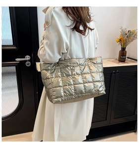 Detail of silver quilted tote bag with gold chain strap and deer charm on beige coat