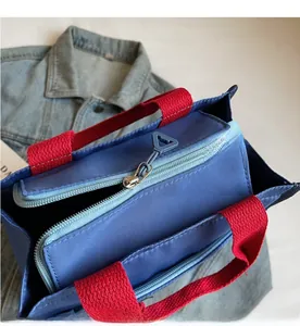 Detail shot of smooth zipper closure and red strap on blue contrast color tote bag