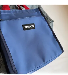 Close-up of blue nylon tote bag with red handles and black FASHION patch detail