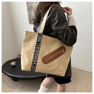 Détail du cabas en toile avec poche en cuir marron et sangles tissées logotypées