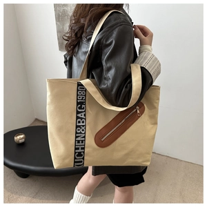 Détail du sac cabas en toile beige avec sangle logo noire et poche zippée en cuir marron