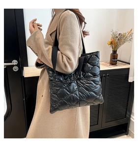 Detail of minimalist black quilted tote bag with smooth finish and wide fabric strap