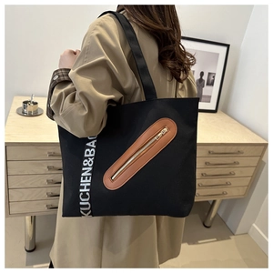 Détail d'un cabas en toile noire avec poche zippée en cuir marron et sangle décorative