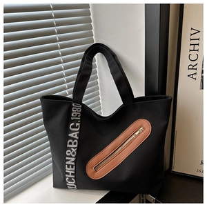 Gros plan d'un cabas en toile noire avec poche en cuir marron et sangle logotypée