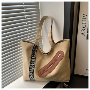 Détail du sac cabas en toile beige avec poche zippée en cuir brun et ruban lettré
