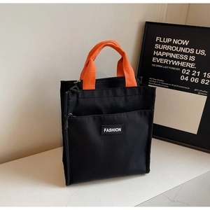 Detail of black tote lunch bag with orange handles and front zipper fashion pocket
