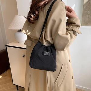 Minimalist black drawstring bucket bag worn over the shoulder with a stylish beige trench coat